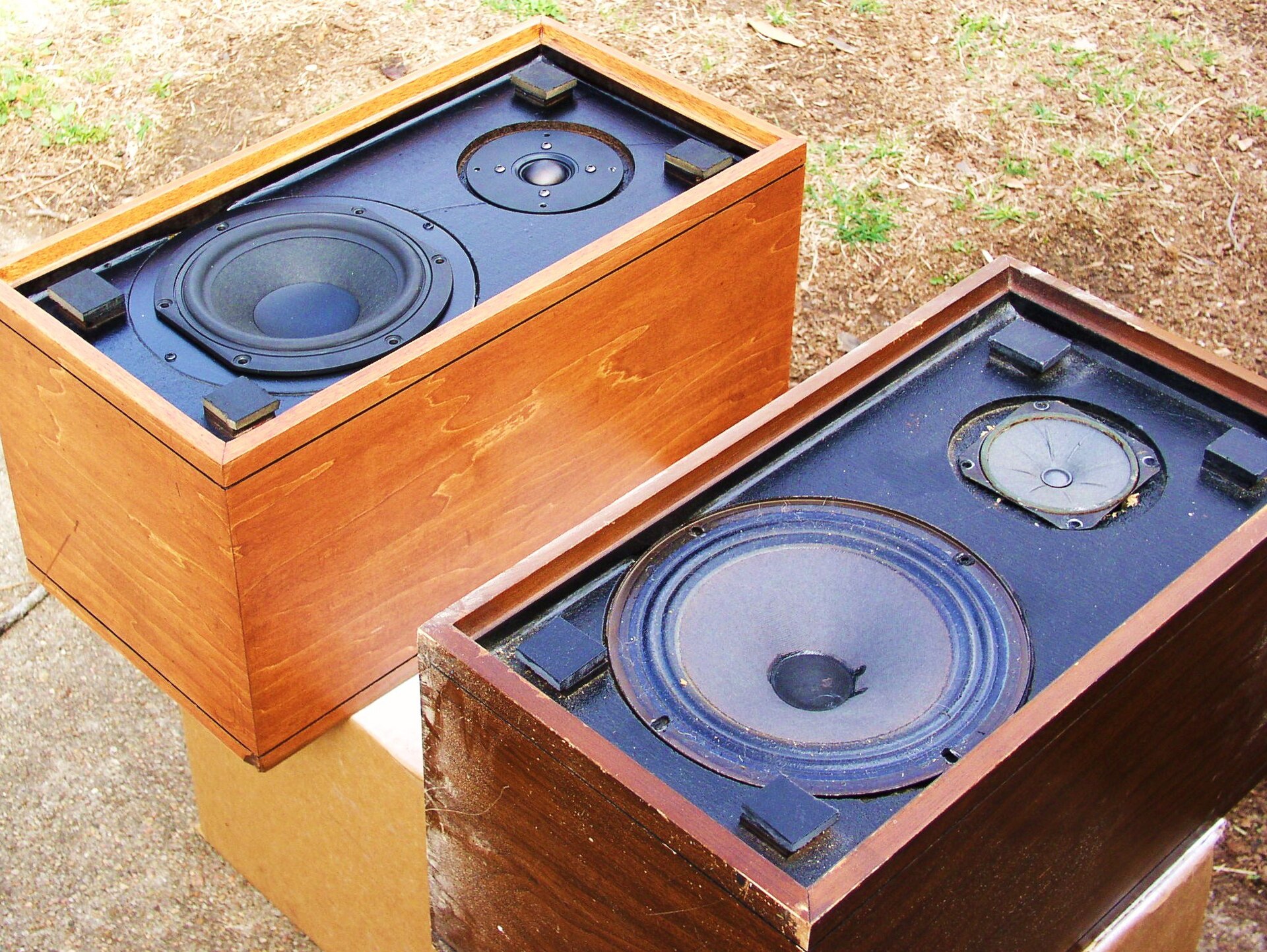 A pair of vintage walnut bookshelf speakers on a wooden shelf with a small Bluetooth adapter beside them